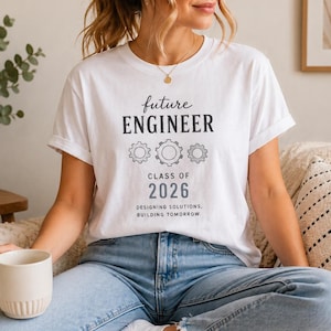 Puede incluir: Camiseta blanca con el texto "future ENGINEER" sobre las palabras "CLASS OF 2026" y la frase "DESIGNING SOLUTIONS. BUILDING TOMORROW." El diseño incluye tres iconos de engranajes. La camiseta se usa con vaqueros azules.