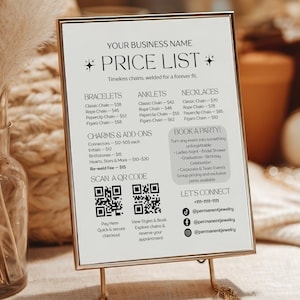Peut inclure: Une liste de prix encadrée en or pour des bijoux, avec des catégories telles que bracelets, chevillières et colliers. La liste comprend des codes QR pour un accès et une réservation faciles. L'affichage est posé sur une table avec des échantillons de bijoux.