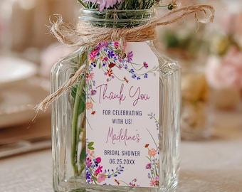 May include: A clear glass vase filled with a bouquet of pink, purple, and white flowers. A decorative tag with the words "Thank You" is tied to the vase with twine. The tag also includes text for a bridal shower.