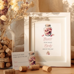 May include: A framed print with the text "Guess How Many Corks Are In The Jar?" is displayed next to a jar filled with corks. Several corks are scattered on the wooden surface. A glass jar with dried flowers is in the background.