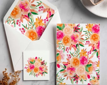 May include: A stationery set featuring a white envelope with a floral interior, a small square card, and a rectangular card. The floral design includes pink, orange, and peach roses with green leaves on a white background. The set is arranged on a marble surface.
