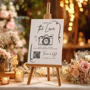 Puede incluir: Un letrero blanco sobre un caballete de madera, con las palabras "CAPTURE the Love" y un dibujo de una cámara. El letrero también incluye el texto "SCAN SNAP SHARE LET'S MAKE MEMORIES TOGETHER!" y los nombres "Tricia & Kyle".