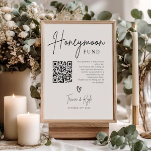 Puede incluir: Un letrero enmarcado con las palabras "Honeymoon Fund" en escritura elegante. El letrero incluye un código QR, un mensaje y los nombres "Tricia & Kyle" con la fecha "October, 25th 20XX". El letrero se muestra en un soporte de madera.