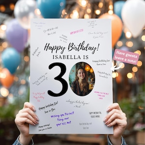 Może przedstawiać: Biały znak urodzinowy z napisem "Happy Birthday!" i "Isabella is 30". Znak zawiera zdjęcie i odręczne wiadomości. Różowe pudełko mówi "Have guests leave a note!"