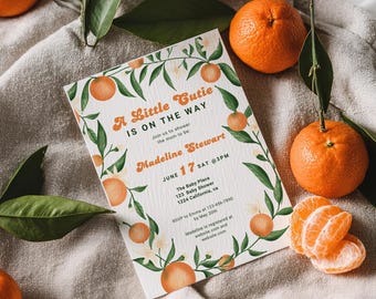 May include: Baby shower invitation with orange and green watercolor design. The invitation reads "A Little Cutie Is On The Way" with details for Madeline Stewart's baby shower. Oranges and leaves surround the text. Several oranges and leaves are scattered around the invitation.