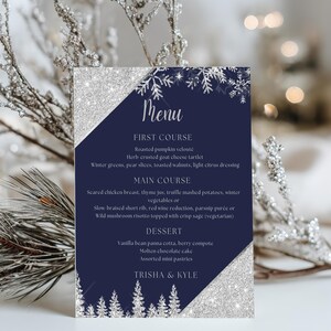 May include: A navy blue menu card with silver glitter accents and snowflake and tree designs. The menu lists a first course, main course, and dessert, with the names of the dishes. The names "Trisha & Kyle" are at the bottom.