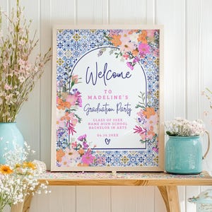Puede incluir: Un cartel de bienvenida para una fiesta de graduación con un diseño floral y un patrón de azulejos azules y blancos. El cartel dice "Bienvenido a la fiesta de graduación de Madeline, Clase de 20XX, Name High School, Licenciado en Artes, 04.16.20XX".