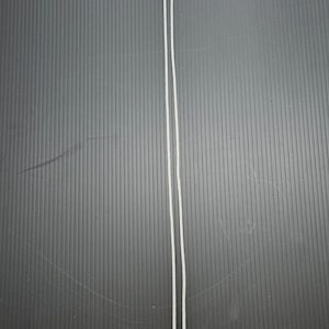 May include: Two thin, white cords are positioned vertically against a dark gray, textured background. The cords are parallel and slightly curved, suggesting flexibility. The image is a simple, clean composition.