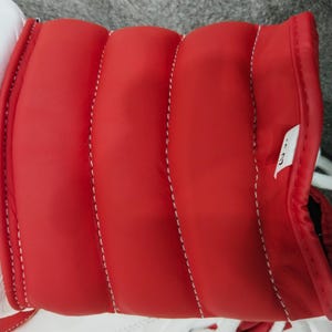 Pu&ograve; includere: Primo piano di una scarpa sportiva rossa e bianca. La scarpa presenta un colletto rosso imbottito con cuciture bianche e una base bianca. I lacci bianchi sono visibili nella parte inferiore dell'immagine.