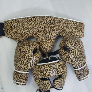 Puede incluir: Conjunto de equipamiento de boxeo con estampado de leopardo. El conjunto incluye guantes de boxeo, protector de cabeza y protector corporal. Los guantes y el casco tienen ribetes blancos. El protector corporal tiene una correa negra.