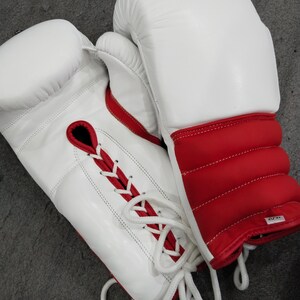 Pu&ograve; includere: Un paio di guantoni da boxe bianchi e rossi. I guantoni sono in pelle e presentano un design allacciato con dettagli rossi. L'area del polso &egrave; rossa con imbottitura. I guantoni sono progettati per la boxe o altri sport da combattimento.