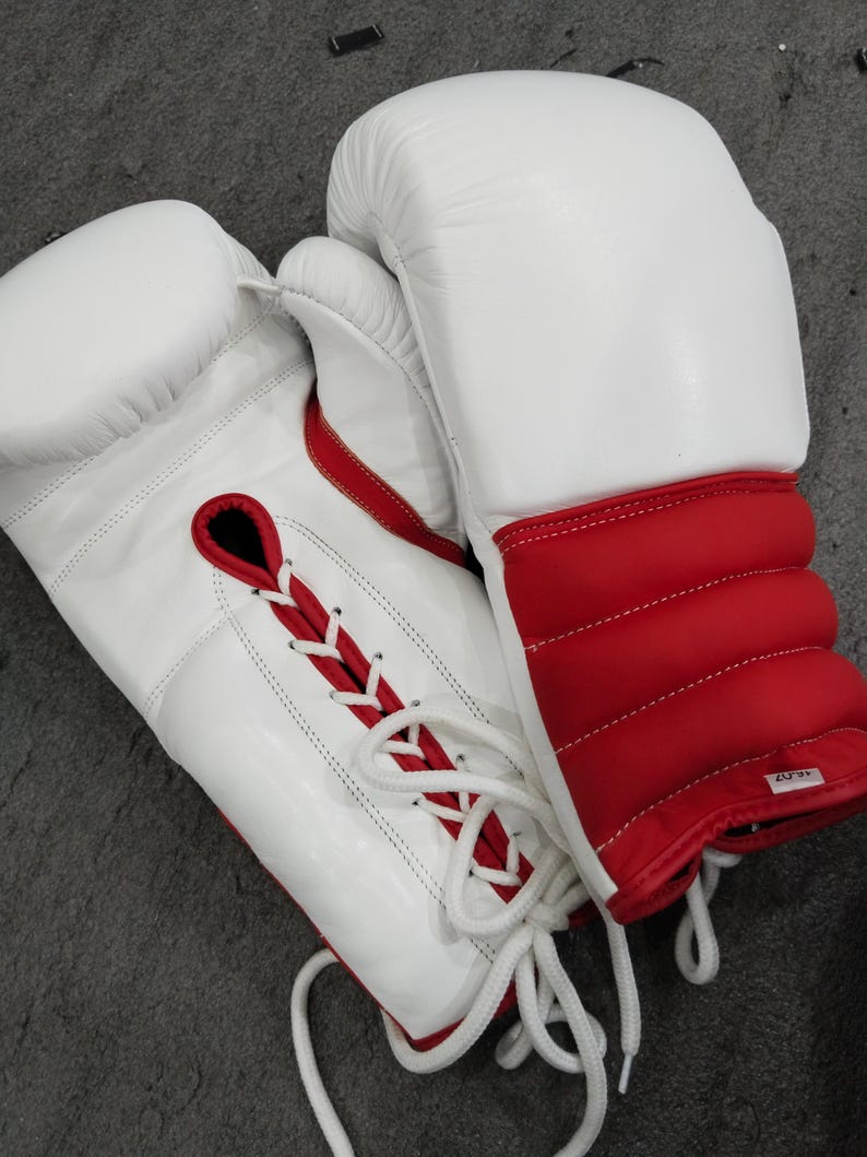 Pu&ograve; includere: Un paio di guantoni da boxe bianchi e rossi. I guantoni sono in pelle e presentano un design allacciato con dettagli rossi. L'area del polso &egrave; rossa con imbottitura. I guantoni sono progettati per la boxe o altri sport da combattimento.