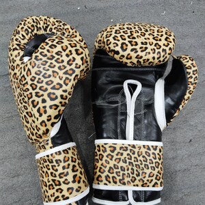 Puede incluir: Par de guantes de boxeo con dise&ntilde;o de estampado de leopardo. Los guantes tienen una base de cuero negro con estampado de leopardo en la parte superior y en la zona de la mu&ntilde;eca. Acentos y costuras blancas completan el dise&ntilde;o.