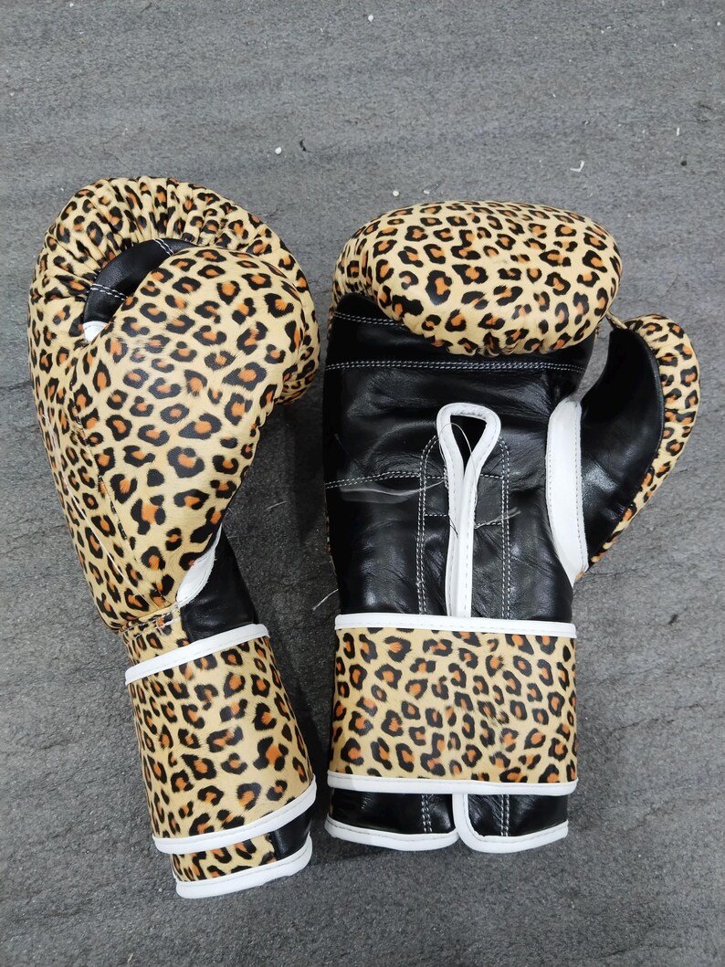 Puede incluir: Par de guantes de boxeo con dise&ntilde;o de estampado de leopardo. Los guantes tienen una base de cuero negro con estampado de leopardo en la parte superior y en la zona de la mu&ntilde;eca. Acentos y costuras blancas completan el dise&ntilde;o.