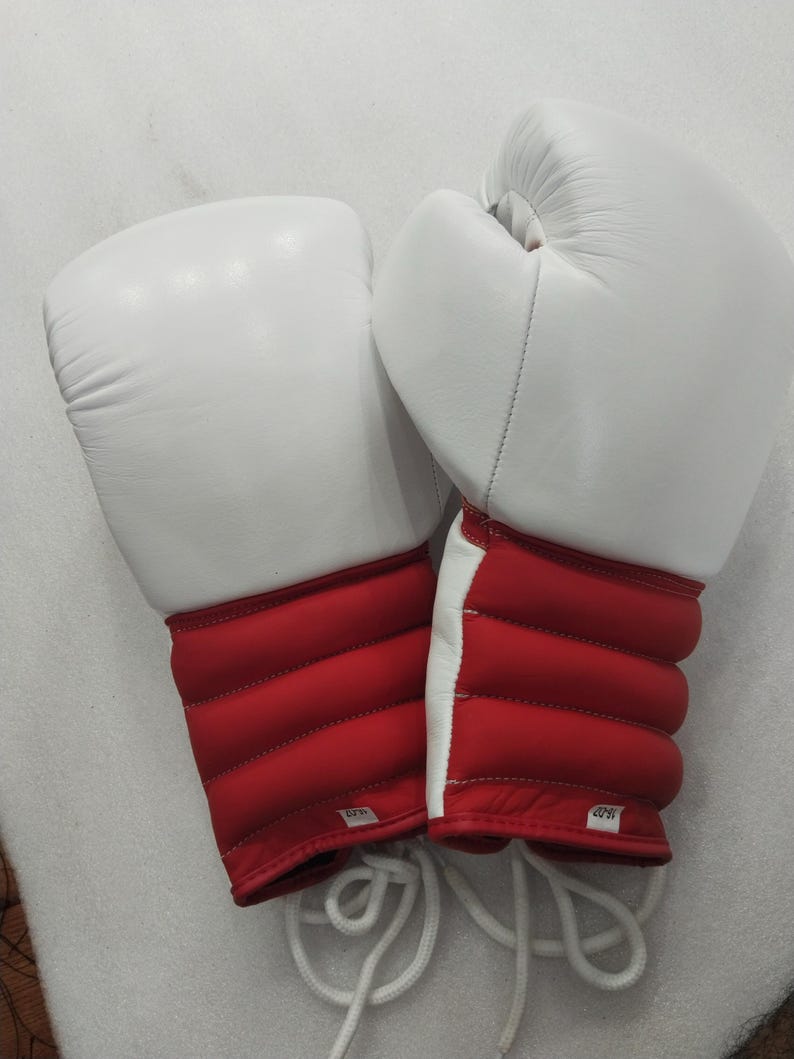 Pu&ograve; includere: Un paio di guantoni da boxe bianchi e rossi. I guanti sono bianchi sulla parte superiore e rossi sulla zona del polso. La zona del polso ha un design trapuntato. Sono visibili lacci bianchi.