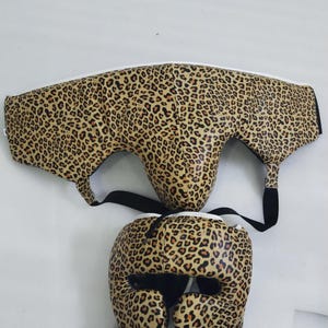 Puede incluir: Juego de protecci&oacute;n de boxeo de dos piezas. El equipo de protecci&oacute;n presenta un estampado de leopardo marr&oacute;n con detalles y correas negras. El casco tiene aberturas para los ojos, la nariz y las orejas.