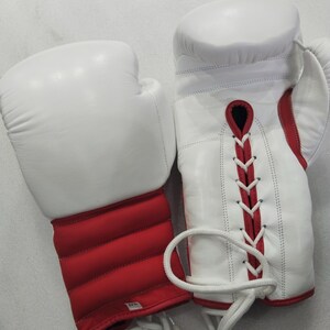 Pu&ograve; includere: Un paio di guantoni da boxe bianchi con dettagli rossi. I guantoni sono in pelle e hanno una chiusura con lacci. L'area del polso &egrave; imbottita e rossa. Progettati per la boxe e altri sport da combattimento.