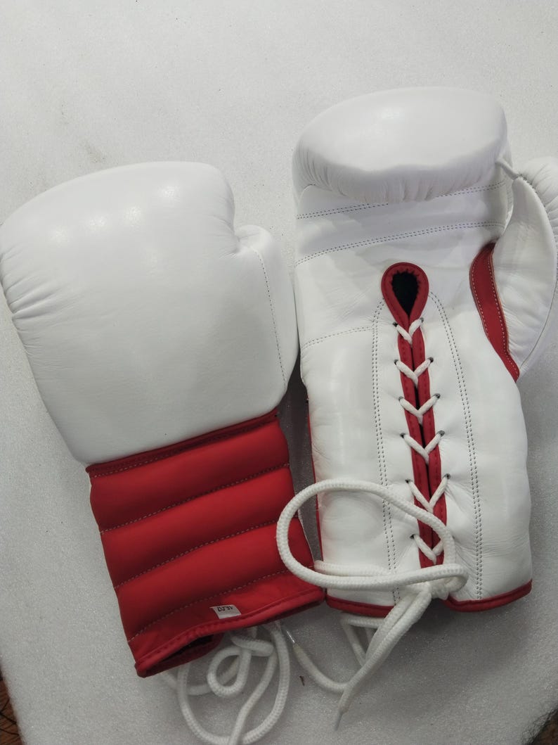 Pu&ograve; includere: Un paio di guantoni da boxe bianchi con dettagli rossi. I guantoni sono in pelle e hanno una chiusura con lacci. L'area del polso &egrave; imbottita e rossa. Progettati per la boxe e altri sport da combattimento.