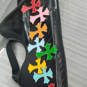 May include: Black leather bag with colorful cross-shaped appliqu&eacute;s in red, pink, orange, light blue, yellow, and green. The bag has a strap and a curved shape, with the letter "M" visible.