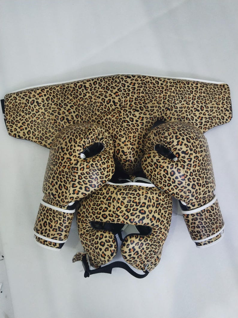 Puede incluir: Un conjunto de boxeo con estampado de leopardo. El conjunto incluye un protector de cabeza, un protector de pecho y guantes de boxeo. Los guantes y el casco tienen acolchado interior negro y ribete blanco.