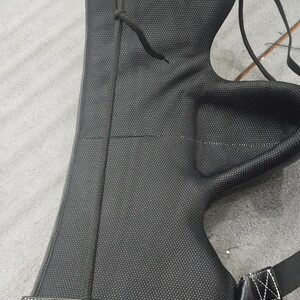 May include: Black archery arm guard with a textured surface and a drawstring. The guard has a padded section and a strap with a white stitched design. The arm guard is designed to protect the forearm.