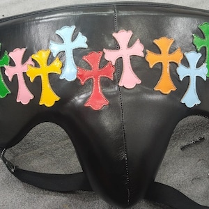 May include: Black leather protective cup with colorful cross appliques. The crosses are in various colors, including green, pink, yellow, and blue. The cup has a contoured shape and adjustable straps.