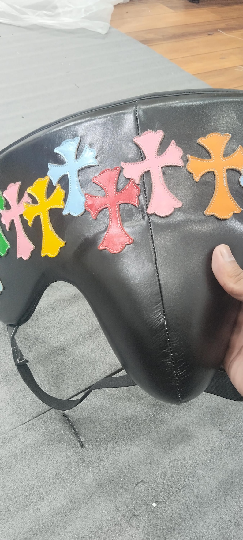 May include: Black leather bag with colorful cross appliques in green, yellow, blue, red, and pink. The bag has a curved shape and a strap. The crosses are outlined in a contrasting color.