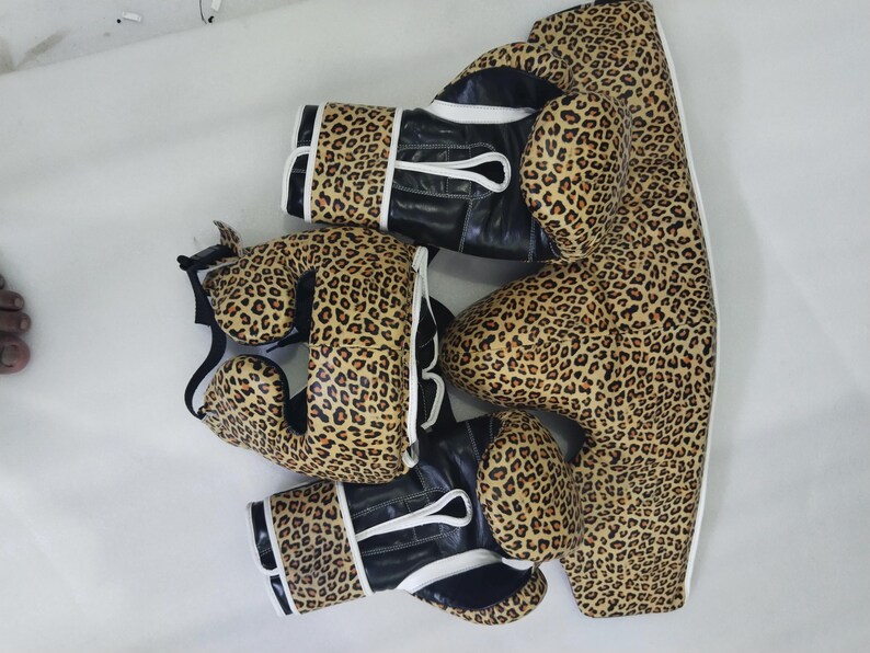 Puede incluir: Un conjunto de equipamiento de boxeo con estampado de leopardo. El conjunto incluye guantes de boxeo, protector de cabeza y protector corporal. Los guantes tienen detalles en cuero negro y ribete blanco.