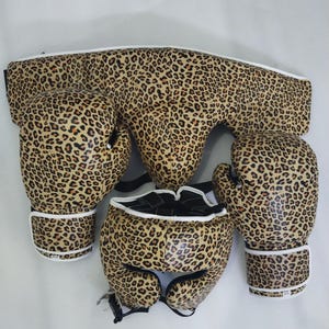 Puede incluir: Un juego de boxeo con estampado de leopardo. El juego incluye un protector de cabeza, guantes de boxeo y un protector de pecho. Los guantes y el casco tienen ribetes blancos. El estampado de leopardo es una mezcla de beige, marr&oacute;n y negro.