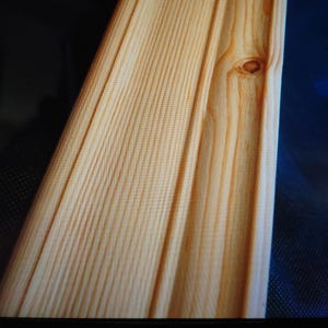May include: Close-up of a light brown wooden trim board with a knot in the centre. The wood grain is visible and the board has a smooth finish.