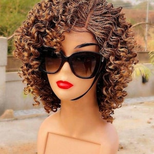 May include: A short curly wig with blonde and brown highlights. The wig is styled with a side part and is worn on a mannequin head. The mannequin is wearing black sunglasses and red lipstick.