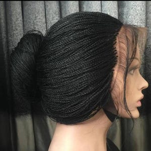 May include: A black braided wig with a lace front. The wig is styled in a bun.