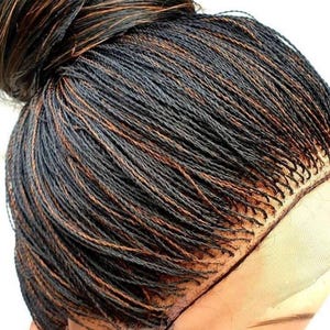 Peut inclure: Une perruque tressée noire et brune avec une dentelle frontale. La perruque est coiffée en un chignon haut.