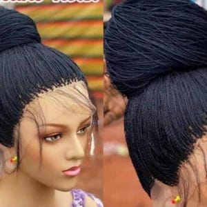 May include: A black braided wig with a high ponytail and a lace front. The wig is styled in a bun on top of the head.