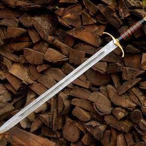 May include: A double-edged sword with a patterned steel blade, a gold-colored crossguard, and a black handle wrapped with thin red bands. The pommel is gold-colored, and the blade features a central fuller running down the length of the metal.