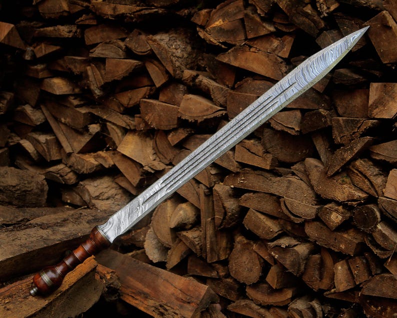 May include: A double-edged sword featuring a patterned Damascus steel blade with a central fuller and a dark brown wooden handle with a rounded pommel. The blade displays a distinct wavy, layered metal texture throughout its length.