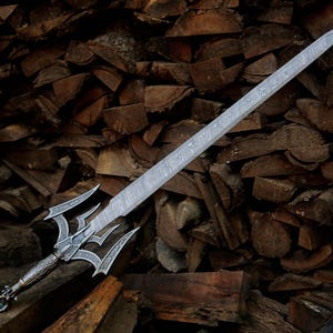 May include: A silver-toned sword featuring a long, double-edged blade with a visible layered metal pattern. The hilt displays intricate engravings, a complex crossguard with multiple pointed prongs, and a textured handle with a decorative pommel.