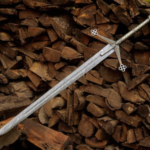 May include: A double-edged sword featuring a distinct wavy Damascus steel pattern on the blade. The silver-toned metal hilt includes a crossguard with four-lobed circular terminals at each end and a textured grip leading to a round pommel.