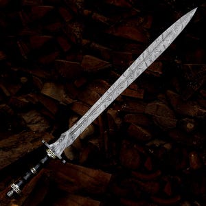 Op de afbeelding: Een tweesnijdend zwaard met een opvallend Damascus stalen lemmet met een wervelend grijs en zilverkleurig patroon. Het gevest is gemaakt van een donker materiaal met goudkleurige metalen accenten en een knop aan de basis van de handgreep.