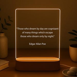 May include: A rectangular LED night light with a quote by Edgar Allan Poe. The light has a brown base and a clear acrylic panel with the quote: "Those who dream by day are cognizant of many things which escape those who dream only by night."