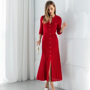 May include: A red knitted dress with a button-down front and a split hem. The dress has a round neckline and three-quarter sleeves. The dress is paired with white heels and a white clutch.