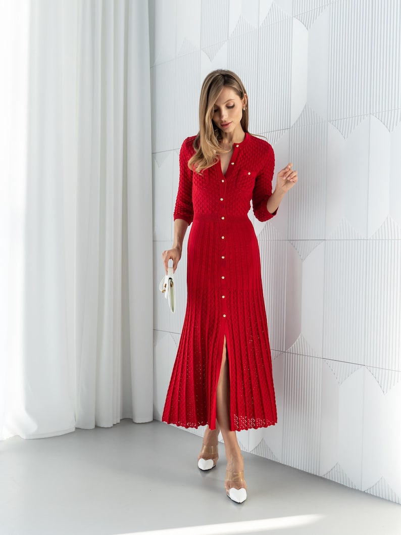 May include: A red knitted dress with a button-down front and a split hem. The dress has a round neckline and three-quarter sleeves. The dress is paired with white heels and a white clutch.