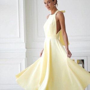 May include: A light yellow halter dress with a flowing skirt. The dress features a bow detail at the back and is knee-length. The model is wearing white heels.