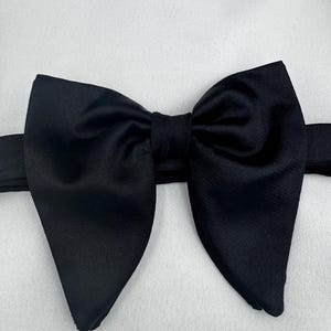 May include: A black bow tie, crafted from a smooth material, sits against a white backdrop. The bow tie is well-tied, featuring a traditional butterfly design, and is suitable for formal occasions and events.