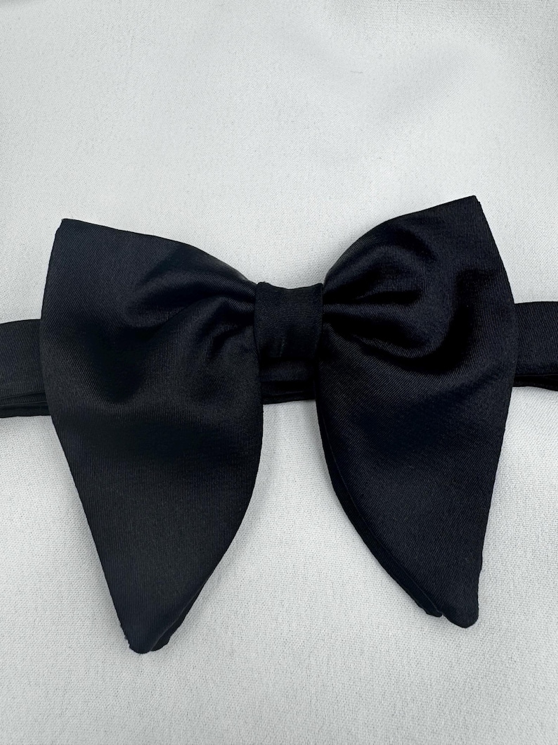 May include: A black bow tie, crafted from a smooth material, sits against a white backdrop. The bow tie is well-tied, featuring a traditional butterfly design, and is suitable for formal occasions and events.