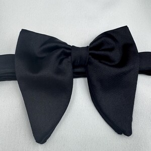 May include: A black bow tie, crafted from a smooth fabric, possibly satin. The image shows the bow tie from above, centered in the frame. This classic accessory is often worn with formal wear, such as a tuxedo or suit.