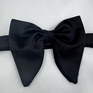 May include: A black bow tie, with a traditional butterfly design. The bow tie is crafted from a smooth, solid black material. The background is a plain white surface.