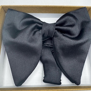 May include: A black bow tie made from a shiny material, presented in a cardboard box. The bow tie is neatly folded and ready to wear. A classic accessory for formal events.