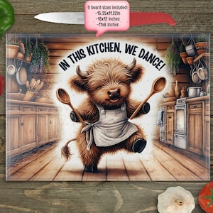 Può includere: Un tagliere rettangolare in vetro con una mucca delle Highlands dei cartoni animati che indossa un grembiule e tiene cucchiai di legno. Il testo "IN THIS KITCHEN, WE DANCE!" è visualizzato. Le dimensioni della tavola includono 39x28cm, 41x30cm e 28x20cm.