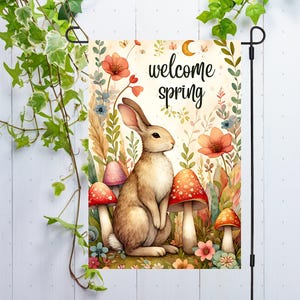 May include: A welcome spring garden flag with a brown bunny rabbit, red and white mushrooms, and the text "welcome spring" in a whimsical font.